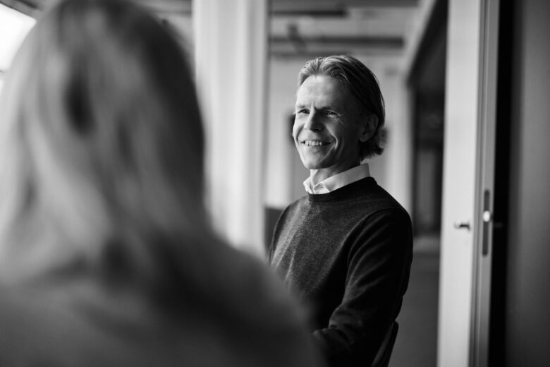 Henkilö katsoo hymyillen toista henkilöä, joka on selin kameraan kuvan etualalla.